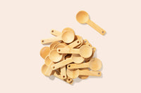 A pile of assorted bamboo spoons lie on a pale pink background.