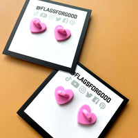 The back of an enamel pride flag pin shows that the stoppers are little pink adorable hearts.