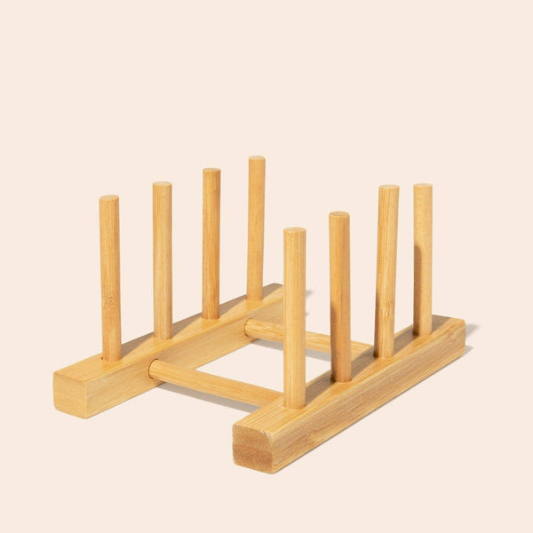 A drying rack made up of bamboo pegs sits against a light pale background. There are four slots in the drying rack for drying dishes or displaying items.