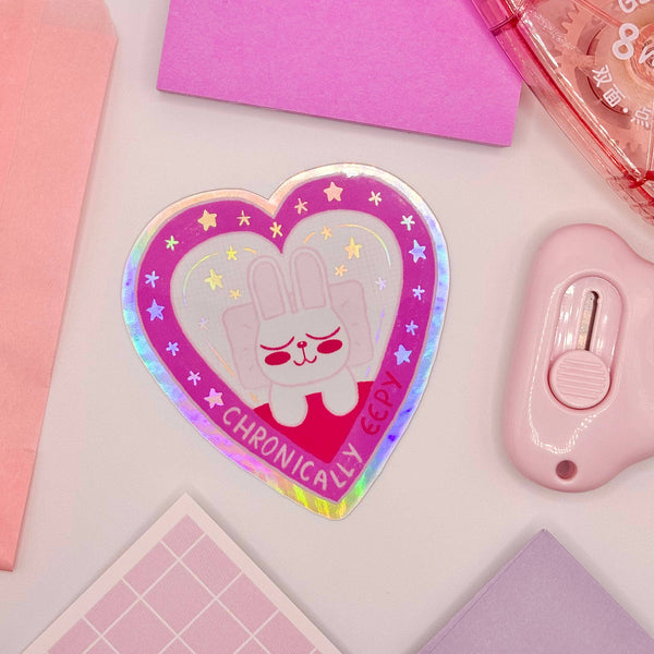A heart shaped cartoony sticker features a cozy sleepy bunny with the words "chronically eepy" underneath.