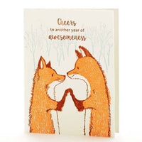 Image shows two foxes on a greeting card holding paws and looking at each other warmly. Text above says "Cheers to another year of awesomeness."