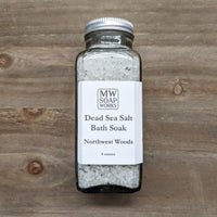 An 8 ounce square bottle of MW Soapworks Dead Sea Salt Bath Soak sits on a wooden background. The scent for the salt is Northwest Woods.