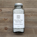 An 8 ounce square bottle of MW Soapworks Dead Sea Salt Bath Soak sits on a wooden background. The scent for the salt is Northwest Woods.