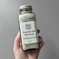 A hand holds up an 8 ounce bottle of MW Soapworks Dead Sea Salt Bath Soak, Calming Lavender scent.