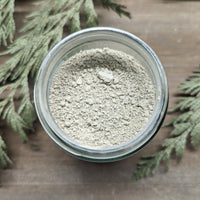 A jar of Deep Clean Clay Mask sits open, showing the light green color of the clays inside.