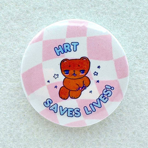 A pin features a cartoon bear that is surrounded by the text HRT SAVES LIVES on a pink checkered background.