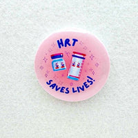 Pink button with HRT Saves Lives written across it with cartoon drawings of pill bottles.