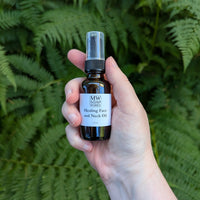 A hand holds a 1 ounce amber bottle of Healing Face and Neck Oil from MW Soapworks
