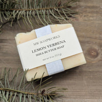 A bar of MW Soapworks Lemon Verbena Shea Butter Soap sits on a natural woodsy background.
