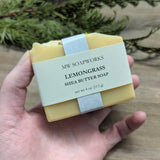 A hand holds a bar of happy yellow Lemongrass Shea Butter Soap from MW Soapworks.