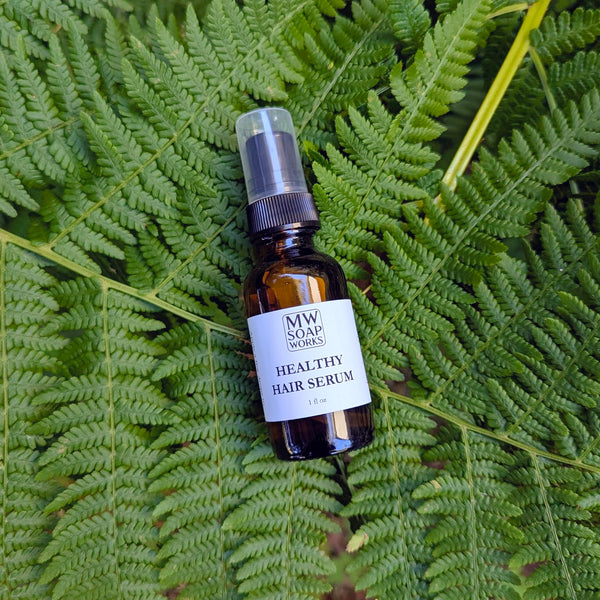 A one ounce amber bottle of MW Soapworks Healthy Hair Serum sits against of background of PNW ferns.