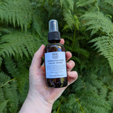 A hand holds a bottle of Hydrating Rose Facial Toner from MW Soapworks against a green fern background