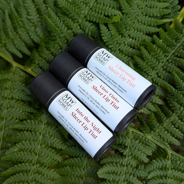 Three compostable paper tubes of MW Soapworks lip tints sit on a lush green bed of PNW ferns.
