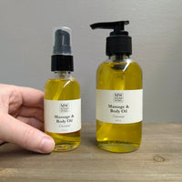 Two clear glass bottles of MW Soapworks Massage and Body Oil sit on a wooden shelf. The bottles contain 2 ounces and 4 ounces of Unscented Massage and Body Oil and have pump lids.