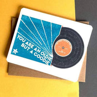 On a yellow and black background, a greeting card has a vinyl record drawing with "you are an oldie but a goodie" next to it.