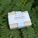 A bar of Orange Spice Shea Butter Soap from MW Soapworks sits on a bed of green ferns.