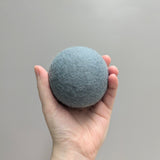 Hand holding a plush light blue wool dryer ball against a gray background