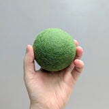 Hand holding a plush green wool dryer ball against a gray background
