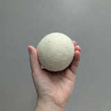 Hand holding a plush white wool dryer ball against a gray background