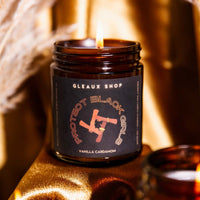 A candle packaged in an amber jar sits on a cozy fall themed table. The label reads "Protect Black Girls"