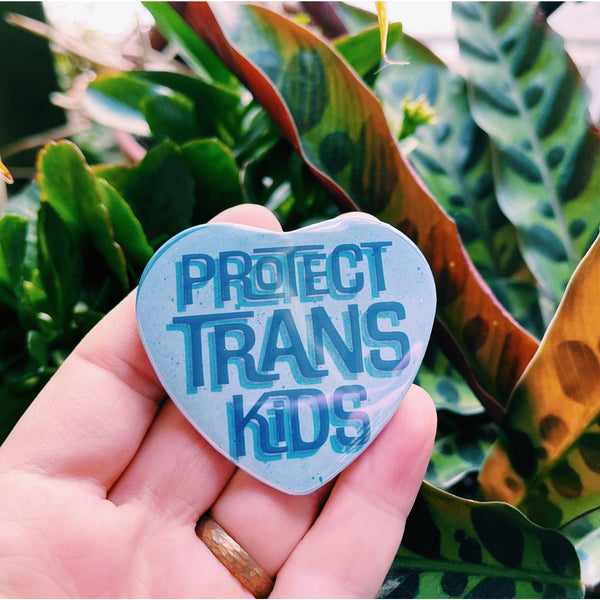 A blue heart shaped magnet reads "protect trans kids."