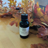 A green one ounce bottle of Pumpkin Spice Fragrance from MW Soapworks sits in front of colorful fall leaves.