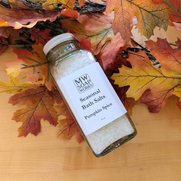 An eight ounce glass bottle of Pumpkin Spice Bath Salts from MW Soapworks sits among colorful fall leaves.