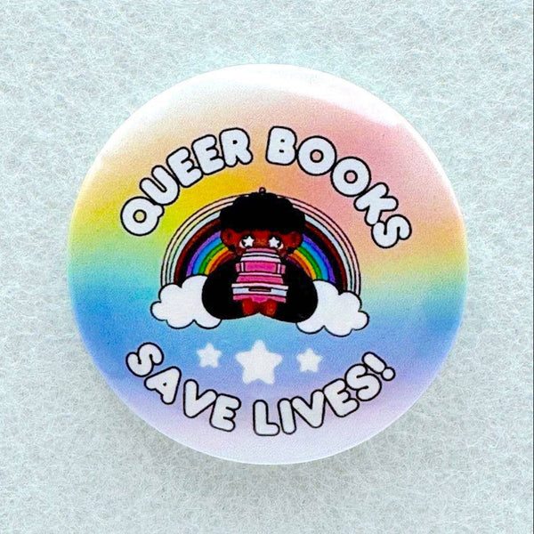 A pin features a cartoon cutie sitting with a stack of books in front of a rainbow and big bubble letters that say "Queer books save lives!"