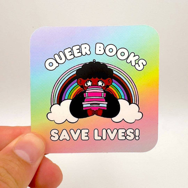 A sticker with a rainbow background features a cartoony cutie holding a pile of books with the words "Queer books save lives!" around them.