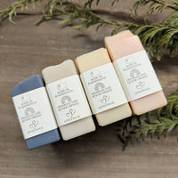 Four types of MW Soapworks soap bars sit on their sides. Logos on this side of the label indicates that they are made in Washington, Disabled and Queer owned, and that the company gives back.