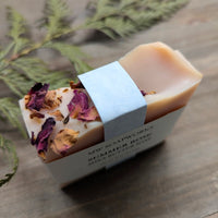 A top view of a Summer Rose soap. The bar is light pink with gentle waves in the top of the soap and pink rose petals along the side.