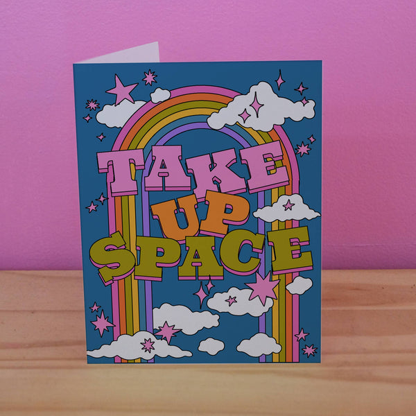 A very colorful greeting card features clouds and rainbows with big block letters that say "Take Up Space."