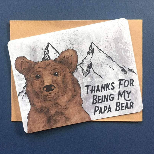 A greeting card sits on a dark blue background. It has a cute bear with text that reads "thanks for being my papa bear."