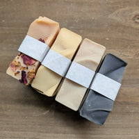 Four MW Soapworks soaps sit on top of a wooden background. The picture shows the subtle waves along the tops of each bar of natural soap.