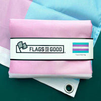 A blue pink and white horizontal striped Transgender Pride Flag sits folded on top of another Trans flag that's been opened.