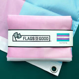 A blue pink and white horizontal striped Transgender Pride Flag sits folded on top of another Trans flag that's been opened.