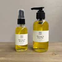 Two clear glass bottles of MW Soapworks Massage and Body Oil sit on a wooden shelf. The bottles contain 2 ounces and 4 ounces of Unscented Massage and Body Oil and have pump lids.