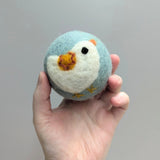 Hand holding a plush wool dryer ball with a cute chicken design against a gray background